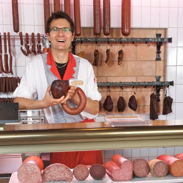 Metzgerei im Allgäu kaufen – Familienbetrieb mit Tradition Metzger im Verkaufsraum einer Traditionsmetzgerei im Allgäu mit hausgemachten Wurstspezialitäten