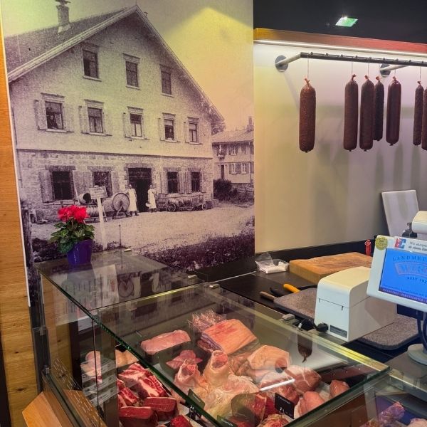 Metzgerei im Allgäu kaufen – Traditionsbetrieb mit Geschichte und moderner Ausstattung Verkaufsraum der Metzgerei im Allgäu mit historischem Wandfoto der ursprünglichen Metzgerei – Verbindung von Tradition und Moderne